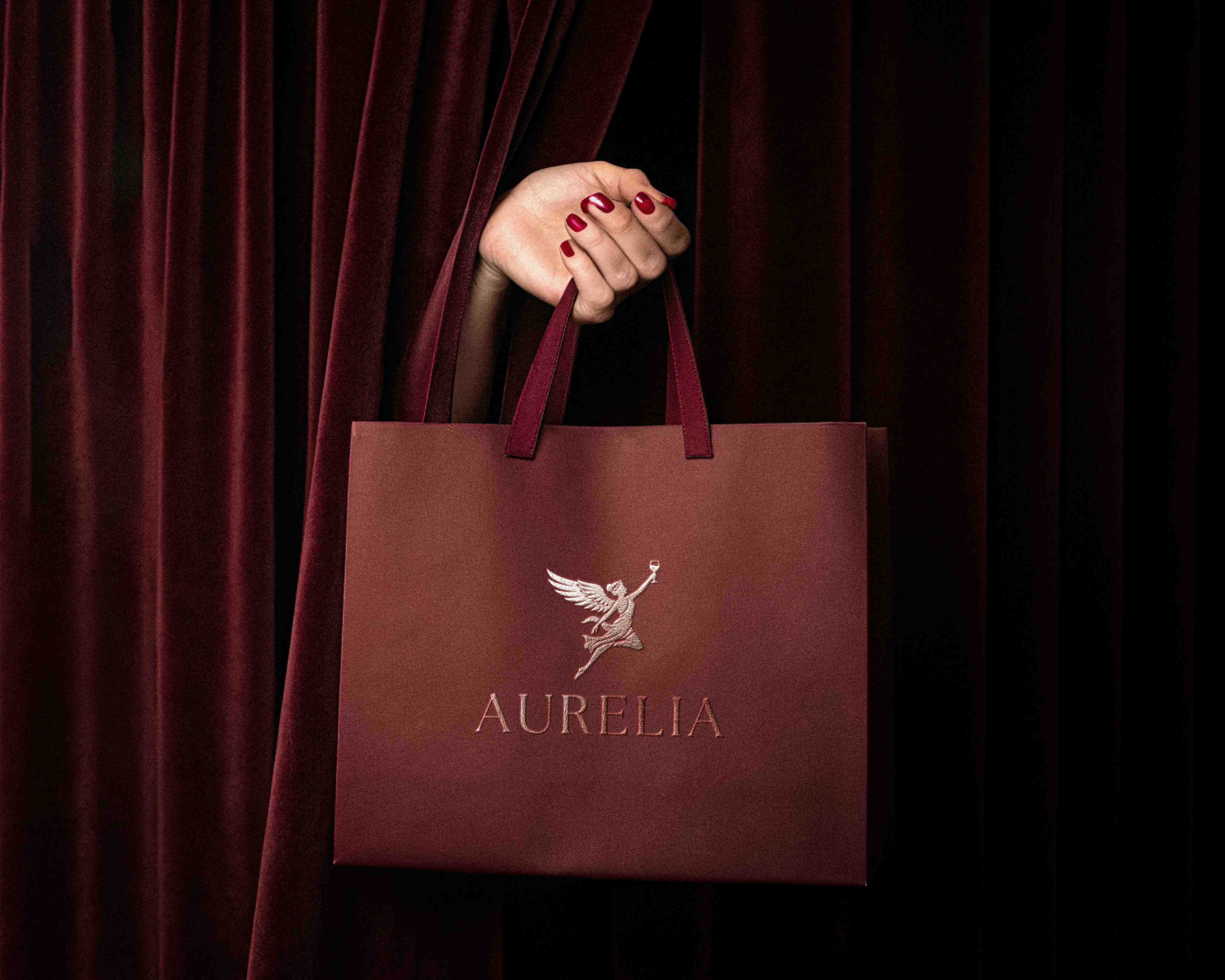 A maroon Aurelia shopping bag held against velvet curtains